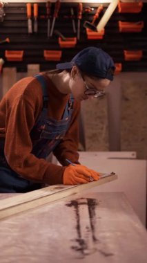 Garaj atölyesindeki kadın marangoz atölyede cetvel ve kalemle ahşap tahtayı ölçüyor..