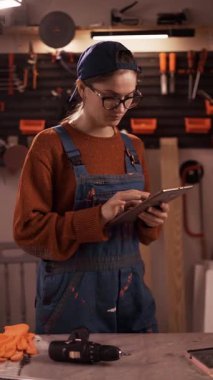 Mobilya tamiri, DIY, ve restorasyon konseptleri. Ev atölyesinde iş tulumu giyen genç bir kadın internetten tablet kullanıyor..