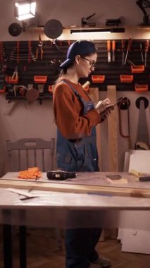 Mobilya tamiri, DIY, ve restorasyon konseptleri. Ev atölyesinde iş tulumu giyen genç bir kadın internetten tablet kullanıyor..