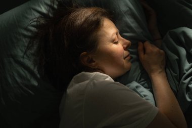 Orta yaşlı bir kadın geceleri yatakta uyuyor. Yukarıdan bak, yatak odasında ortopedik yastık var. Boşluğu kopyala