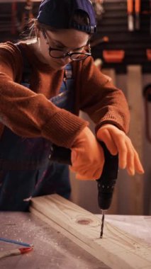 Dişi marangoz ya da turuncu eldivenli bir katılımcı ahşap kalaslarda delik açıyor. Marangozluk atölyesinde tahta delme işlemi. Boşluğu kopyala