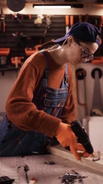 Keresteye vida sokmak için elektrikli tornavida kullanan kadın marangoz. Bir atölyede ahşap işleme süreci.