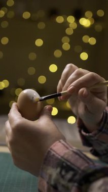 Kadın eli, arka plandaki bulanık çelenk ışıklarıyla yumurtaları beyaz boyayla boyuyor. Paskalya, tatiller ve insanlar konsepti