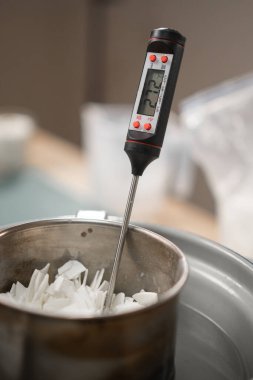 Ev yapımı mumlar yapmak için termometreyle eritilmiş soya cilasının sıcaklığını ölçüyorum. yakın plan