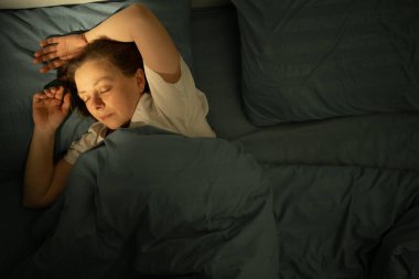 Orta yaşlı bir kadının pamuklu çarşafların üzerinde sıcak bir battaniyenin altında huzurlu bir şekilde uyuduğu en iyi manzara. Ev konforu, rahatlama, derin uyku ve rahat atmosfer kavramı.