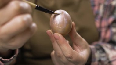 Kadın eli, paskalya yumurtasını fırçayla gümüş rengine boyuyor. Paskalya, gelenekler, tatiller ve insanlar konsepti. yakın plan