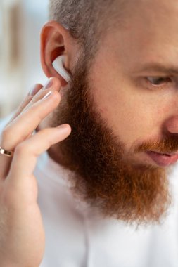 Kablosuz kulaklık kullanan sakallı adam. Müzik dinliyordum. Kulaklıkları kulaklığa yakın çekim. Boşluğu kopyala