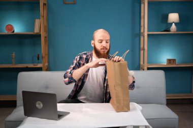 Sakallı adam öğle yemeği molası verdi. Paketlerden yemek siparişi verdi. Yemek siparişi verdi. Tüketim, yeme ve insanlar konsepti. Yemek dağıtım servisi. Boşluğu kopyala