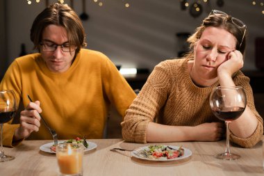 Evli çift mutfakta geç saatte yemek yiyor. Yorgun bir eş masada uyurken, sıkılmış koca yakınlarda oturuyor. Aile içi ilişki sorunu, yorgunluk, duygusal mesafe, rutin