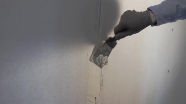 Erkek eli sıva duvarına sıva yapıştırmadan önce spatula kullanarak sıva koyuyor, vida deliklerini dolduruyor. Duvarın macun işlemesi. Boşluğu kopyala