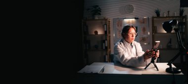 A female doctor communicates with a patient via video call using a smartphone while working the night shift at a hospital. banner. copy space