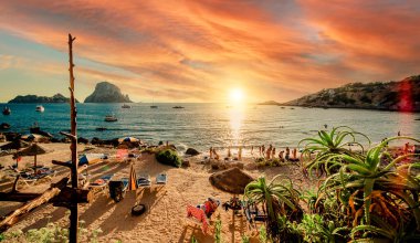 Cala d 'Hort tropikal plajının muhteşem manzarası. İnsanlar muhteşem, canlı günbatımında Es Vedra kaya manzarasıyla güzel plajlarda takılıyor. Balear Adaları, İspanya, Espana. İbiza