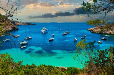 Yelkenliler, Cala Salada gölüne demirlediler. Idyllic manzara, bulutlu gökyüzü arkaplanı. İbiza, Balear Adaları. Avrupa. İspanya