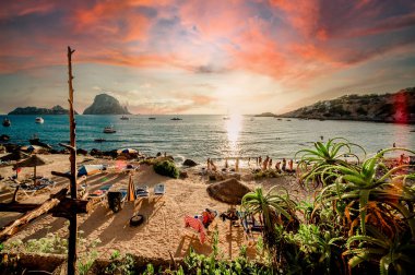 Cala d 'Hort tropikal plajının muhteşem manzarası. İnsanlar muhteşem, canlı günbatımında Es Vedra kaya manzarasıyla güzel plajlarda takılıyor. Balear Adaları, Espana. İbiza