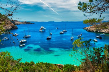 Çamurlu gemiler, yelkenliler, yatlar, Cala Salada turkuaz lagün koyundaki motorlu botlar. Tatilciler ve yaz tatilleri için ideal bir yer, parlak renk, İbiza Adası, Balear Adaları. İspanya