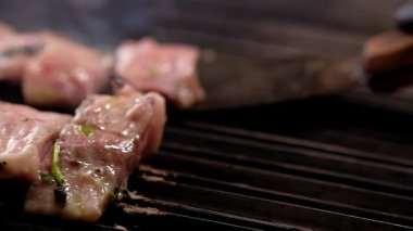Şef, ızgaranın sıcak yüzeyi üzerinde metalik spatulası olan terbiye edilmiş cerrahları hareket ettiriyor. Kaydırmalı kamerayı yavaş çekimde hareket ettiriyor, balık dilimlerini kapatıyor, pişirme işlemi yapıyor.