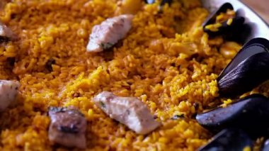 Paella geleneksel İspanyol mutfağını yakın çekim videosu, şefin deniz ürünleri tabağını çelik maşayla süslemesi mersin balığı filetosu dilimleri...