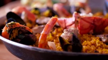 Paella 'yı limon dilimiyle dekore eden şefin siyah eldiveni, videoyu yakın çekim, hazırlanmış İspanyol geleneksel paella mutfağının olgun malzemeleri.