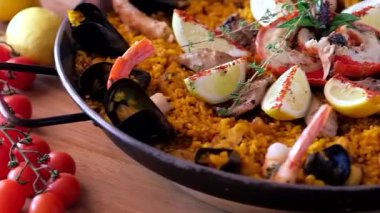 Büyük, sığ bir tavada, güzel dekore edilmiş ve yenmeye hazır deniz ürünleri paella 'sı.