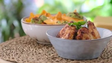 Üst tarafta yavaş çekimde tavuk kanadı ve guacamole soslu kızarmış patates cipsi servis ediliyor.