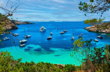 Cala Salada lagünündeki yelkenliler. Parlak yeşil deniz manzarası, bulutlu gökyüzü, Idyllic manzarası. İbiza, Balear Adaları. Spai.