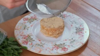 Tanınmayan erkek aşçı elleri süzgeç süsleme ballı kek porsiyonuna pudra şekeri serpiştirir, manzara tabağını ve tatlıyı kapatır. Restoran yemeği hazırlama konsepti