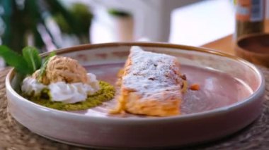 Elmalı turta, geleneksel Viyana turtası üzerine pudra şekeri serpiştirilmiş nane yaprağıyla süslenmiş dondurma topları, dönen tabağa yakın görüş. Restoran tatlı yemeği konsepti.