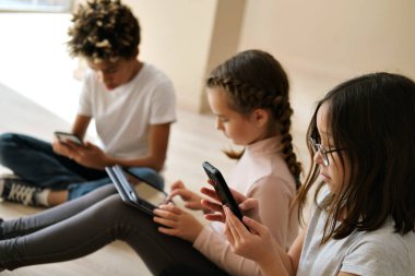 Üç tane çok ırklı Afrikalı, Kafkas ve Koreli küçük çocuk kablosuz aygıtlarla içeride oturuyor. Modern teknoloji akıllı telefonların aşırı kullanımı, genç Alfa üretimi kavramının dijital cihazları