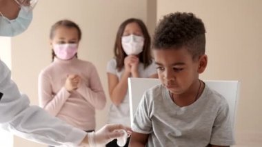 Beyaz önlüklü, koruyucu yüz maskesi takan kadın doktor elinde şırıngayla küçük Afrikalı çocuğa aşı yapıyor. Koronavirüs salgınına karşı doz. Covid konseptine karşı aşı