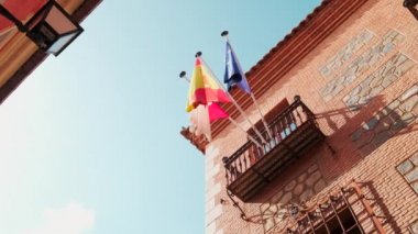 Turistik Toledo kasabasının eski binasında bayrak direğinde üç bayrak sallanıyor. CastillaLa Mancha, Avrupa Birliği ve İspanya bayrağı, güneşli bir günde mavi gökyüzüne karşı görüş. Avrupa. İspanya
