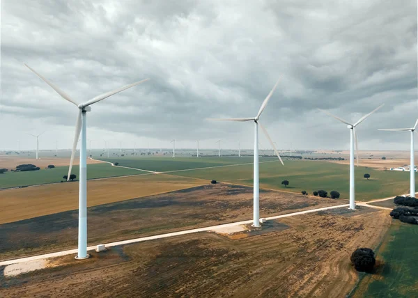 Drone point of view turbines of windmills. Wind energy converter into electricity. Panoramic of cultivated farm lands during gloomy day, cloudy sky. Europe, Spain