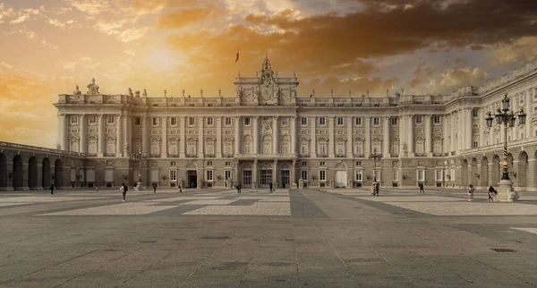 黄金の夕日曇りの空の背景に対するマドリードの王宮の建物の外観 認識できない人々が広場に沿って歩く マドリード市内の広場 旅行先のコンセプト スペイン — ストック写真