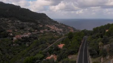 Akdeniz kıyısındaki yeşil dağlar boyunca uzanan dolambaçlı bir yol, insansız hava aracı bakış açısı. Palma de Mayorka. Balear Adası, Avrupa. İspanya