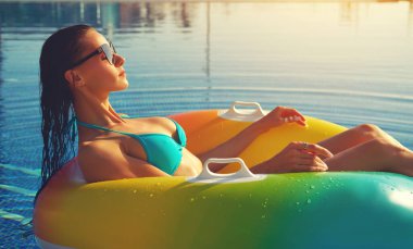 Yüzme havuzunda sakin 30 'lu yaşlarda kadın güneş gözlüğü takıyor ve bikini giysisi kauçuk çemberin içinde oturuyor. Güneş yanığı, cilt bakımı, krem rengi UV koruması, yaz tatili, tatil beldesi, rahatlama konsepti
