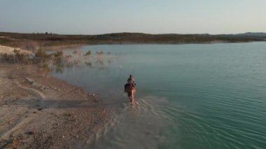 İnsansız hava aracı bakış açısıyla genç beyaz kadın Orihuela 'daki La Pedrera Gölü manzarasında ata biniyor. İspanya. Hobi, binicilik sporu ve aktif yaşam tarzı kavramı