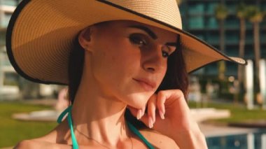 Bikinili, güneş gözlüklü, saman şapkalı, yüzme havuzunun yanında poz veren akıllı telefonlu bir kadın yaz tatilinin özçekim fotoğrafını çeker. Yaz tatili, modern teknoloji, güzellik konsepti