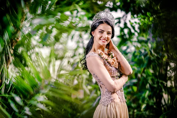 Elegant leende dam med tiara på ett huvud som poserar i en skog — Stockfoto