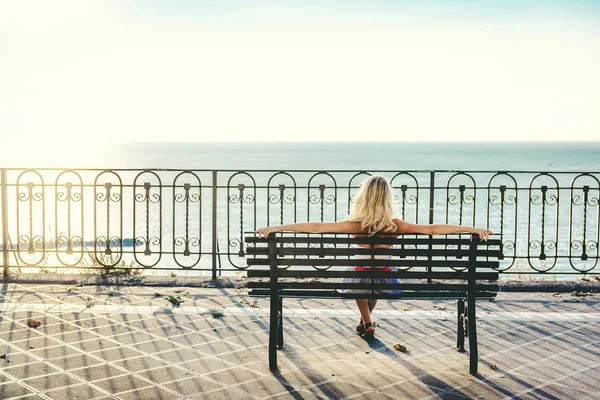 ベンチに座っていると、海で探している金髪の女性 — ストック写真