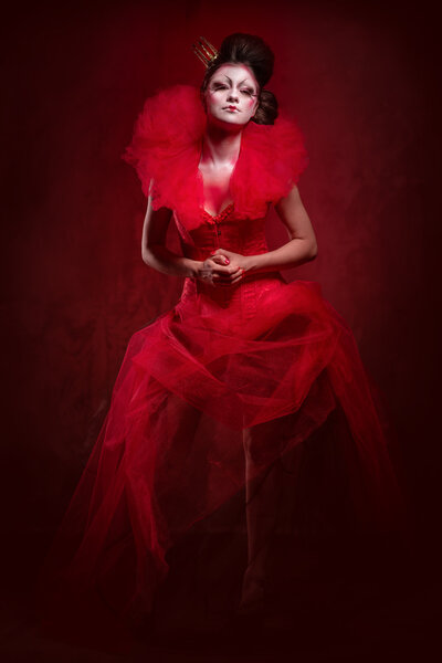 Red Queen. Woman with creative make-up in fluffy red dress posing indoors