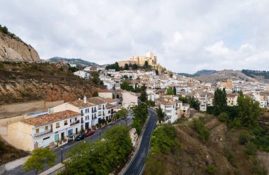 Panoramic view of Velez-Blanco picturesque village, aerial view of houses clustered along winding streets, with impressive 16th-century Castillo de Velez-Blanco perched atop hill. Southern Spain