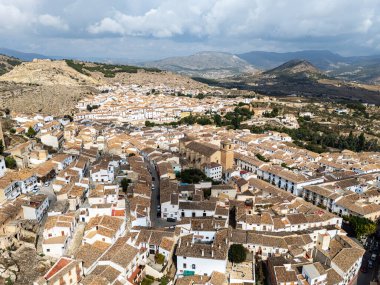 Scenic aerial view of historic town of Velez-Blanco in southern Spain, traditional whitewashed houses, central church, and dramatic mountain landscapes in background