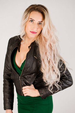 Uzun saçlı, yeşil elbiseli ve siyah deri ceketli bir sarışının portresi.