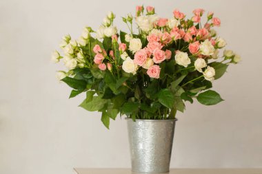 Masadaki vazoda küçük, narin pembe ve kremalı güller.