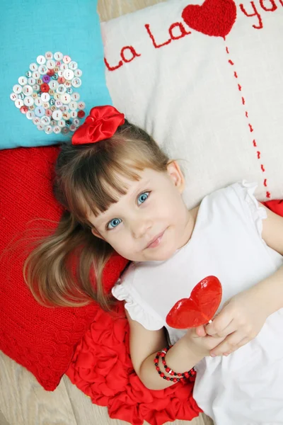 Girl on the pillows holding a lollipop — Stock Photo, Image