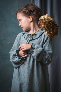 Genç bir kız ortanca çiçekli bir dal tutuyor. Yeşil bir elbise ve bir tasma giyiyor..