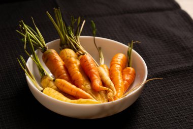 Parlak turuncu ve soluk sarı havuçlar koyu siyah bir kumaşa karşı canlı bir şekilde öne çıkarak doğal güzelliği ve taze otantik çiftliği vurguluyor. Sağlıklı yaşam tarzı ve yavaş yemek için uygun.