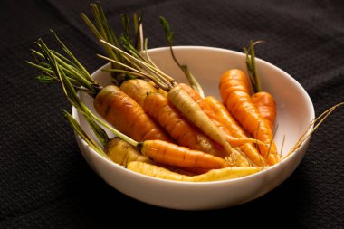 Bir kenar açı, karamsar bir çiftlik için siyah bir kumaş üzerinde kökleri ve tepeleri olan taze toplanmış havuçları ön plana çıkarıyor. Bitkisel yemek ve yavaş yaşam ilhamı için mükemmel.