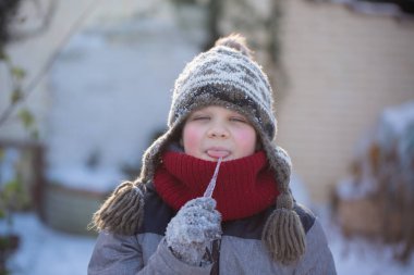 Kış şapkalı bir çocuk dışarıda buz sarkıtı tadıyor, çocukluktaki merak, neşe ve farkındalığı temsil ediyor..