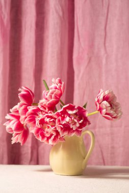 Seramik bir sürahide pembe laleli fotorealistik natüralistik natüralistik yaşam yumuşak kumaş arka planda, zarif doğal ışık ve sakin atmosfer, anneler günü, doğum günü, doğum günü, kutlama, tebrik kartı, ev dekorasyonu ve yaşam tarzı kullanımı için uygun.