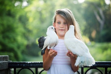 Genç kız iki beyaz güvercini nazikçe açık havada, yumuşak doğal ışıkta tutuyor. Barışın sembolü, şefkat, çocukluk masumiyeti, duygusal bağ, hayvanlara ve doğaya ilgi..